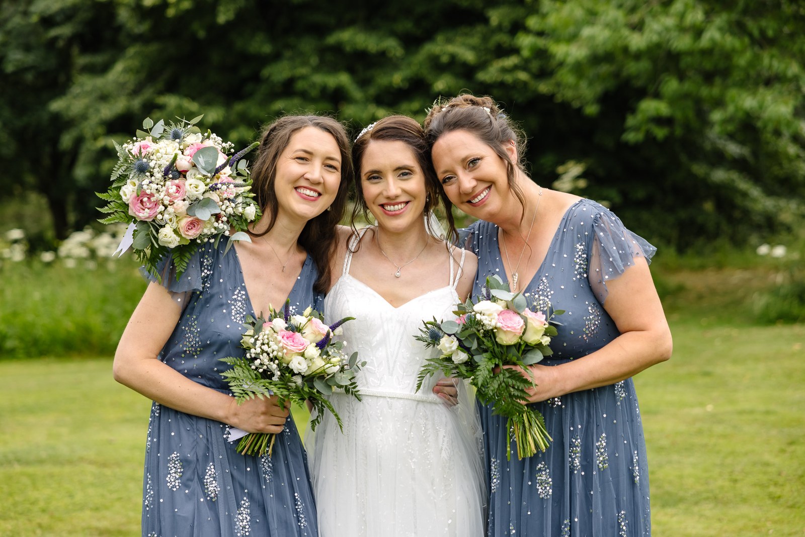 The bride flanked by two bridesmaids in blue, all holding bouquets