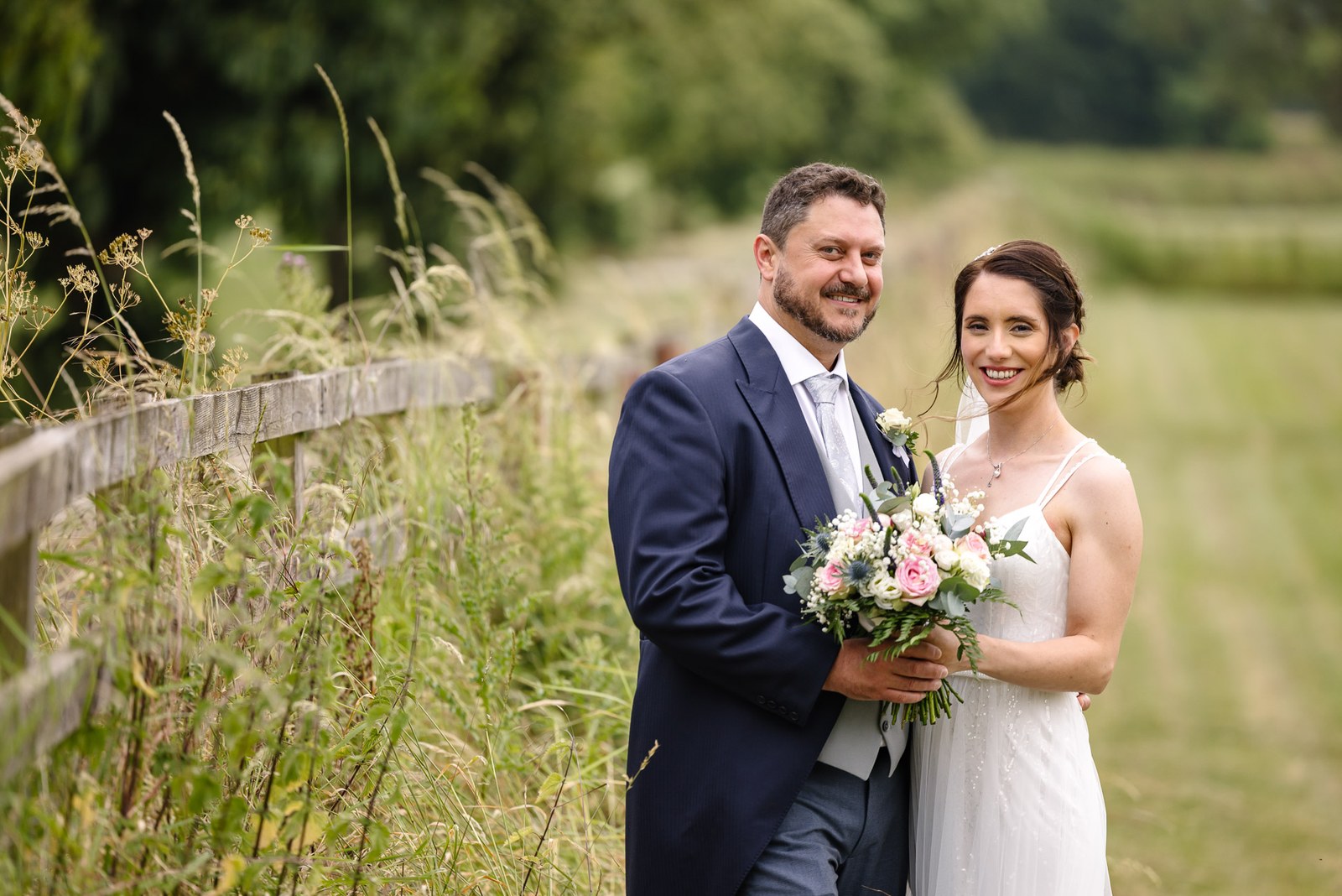 The couple embrace by a wooden fence in the meadows of Crockwell Farm