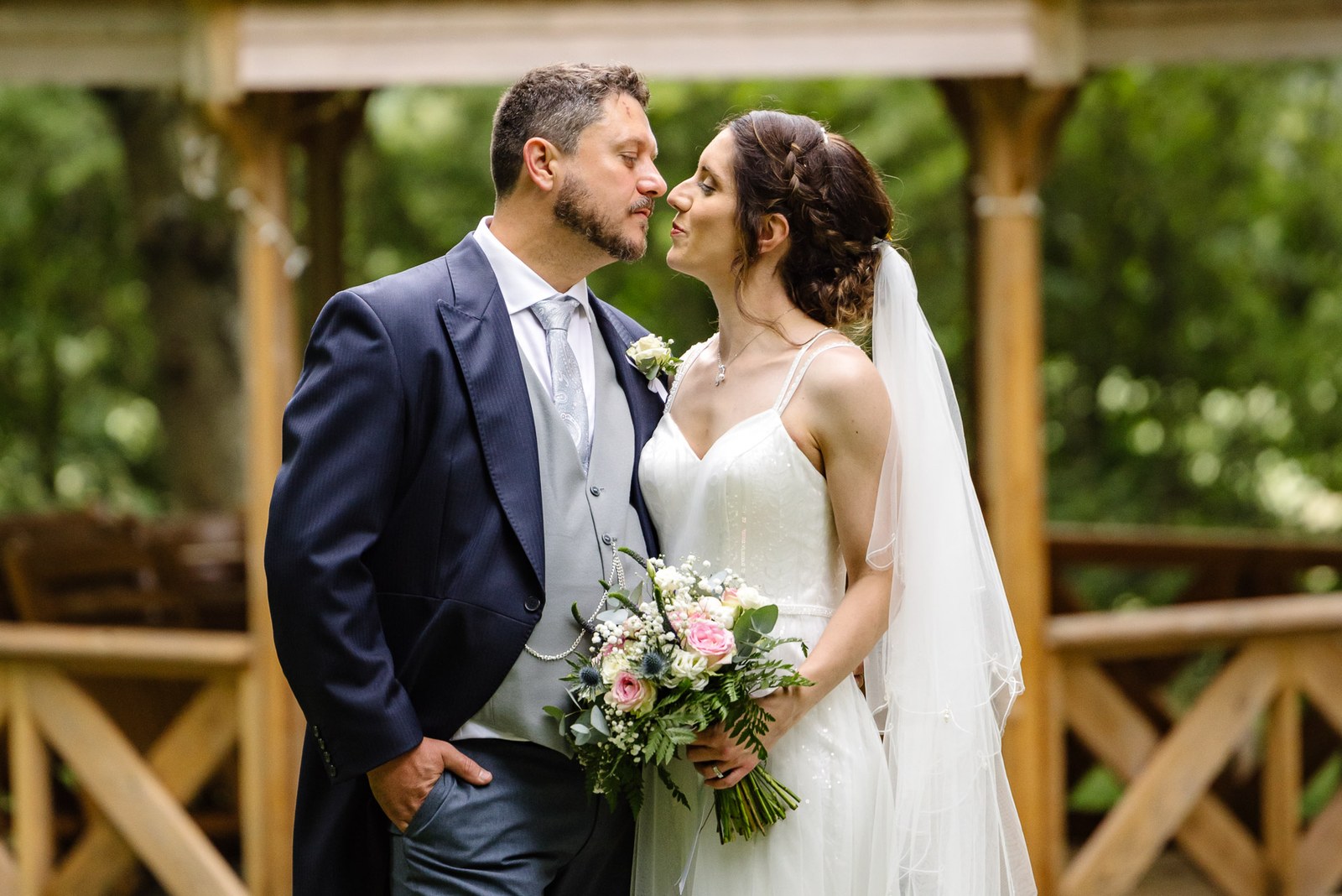 The couple pause together beneath a rustic wooden pergola