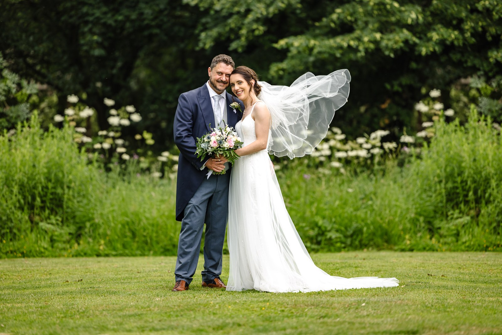 The bride's veil lifts on the breeze as the couple stand on the lawn at Crockwell Farm