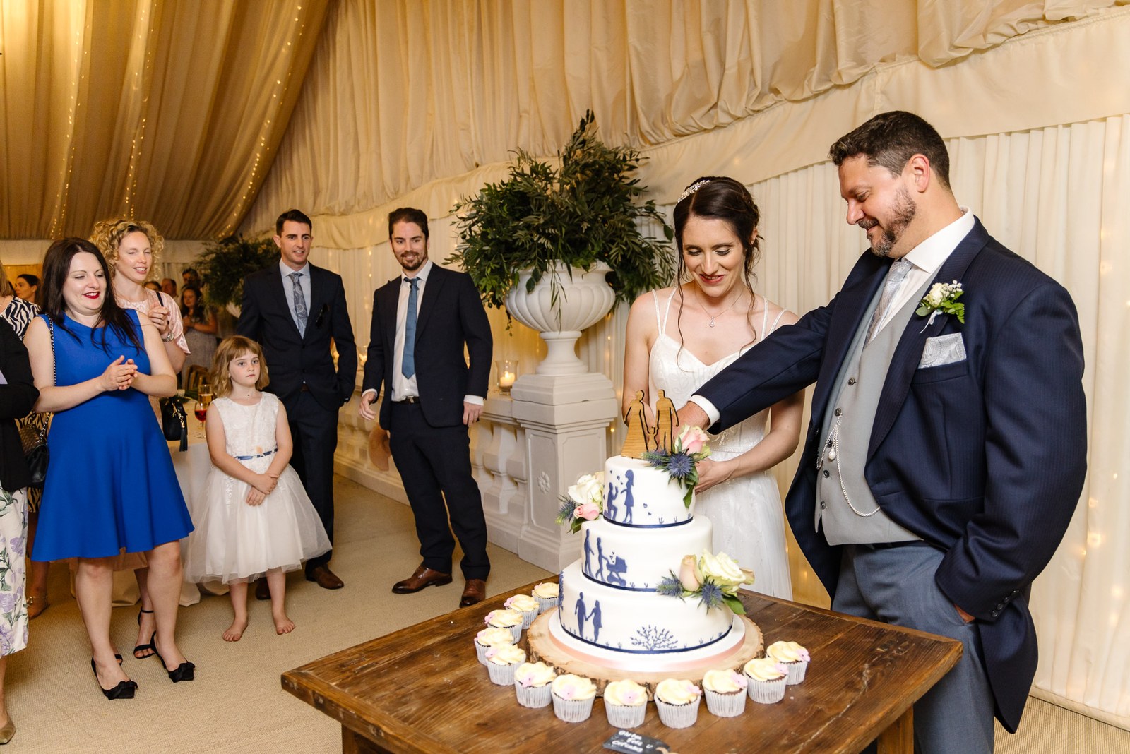The couple cut their tiered cake in the marquee as guests gather round