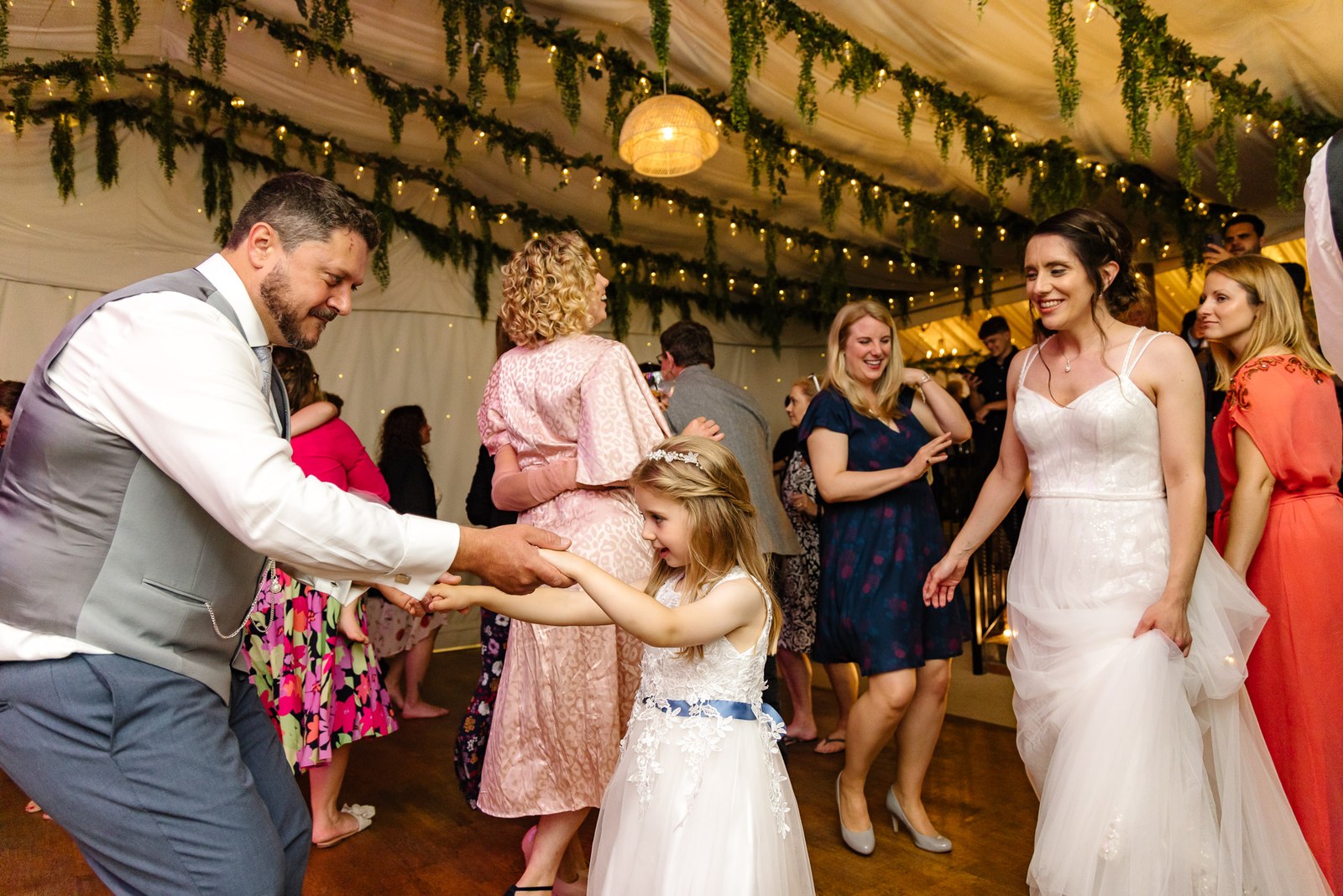 Guests dance together in the marquee, a flower girl joining the couple