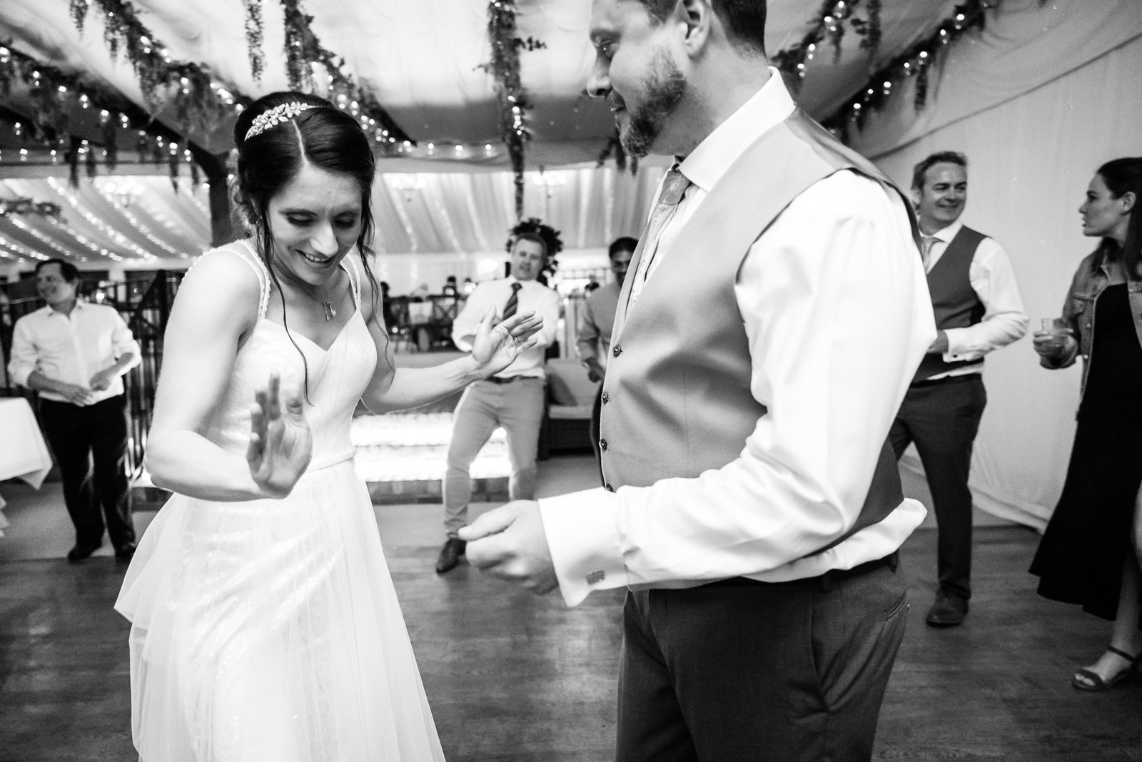 Black-and-white shot of the couple dancing among guests in the marquee