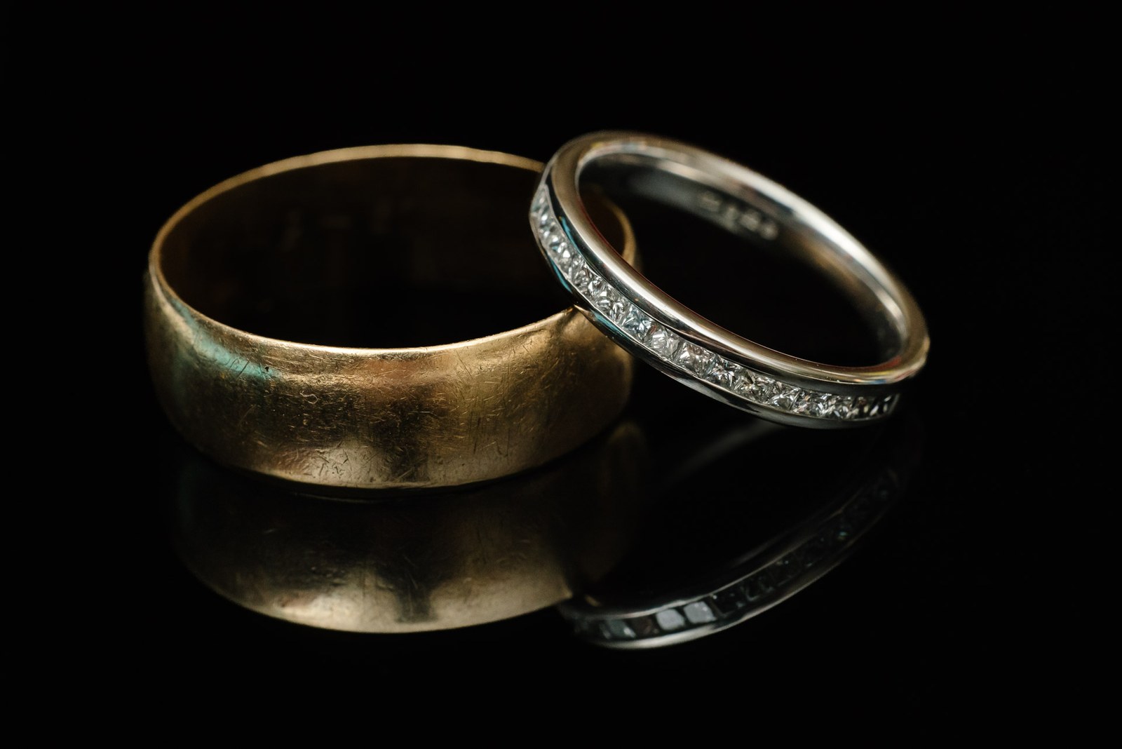 Close-up of a gold band and a diamond eternity ring on a black surface