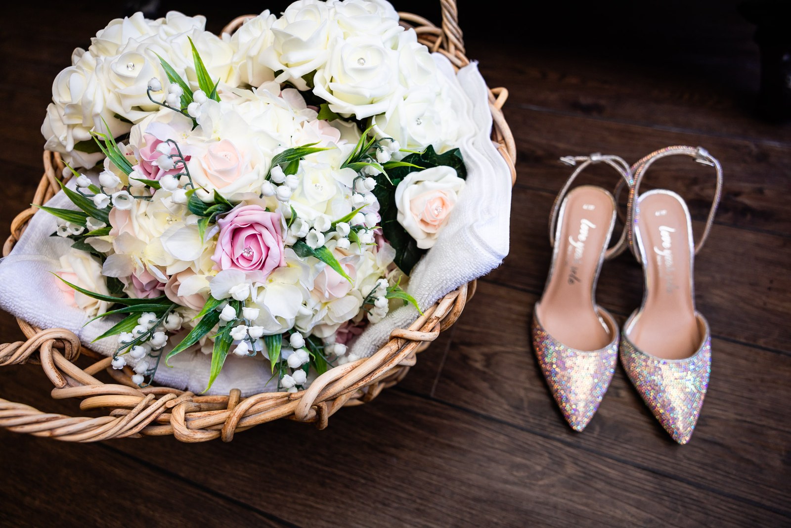 The bride's white and pink rose bouquet in a basket beside glittery heels