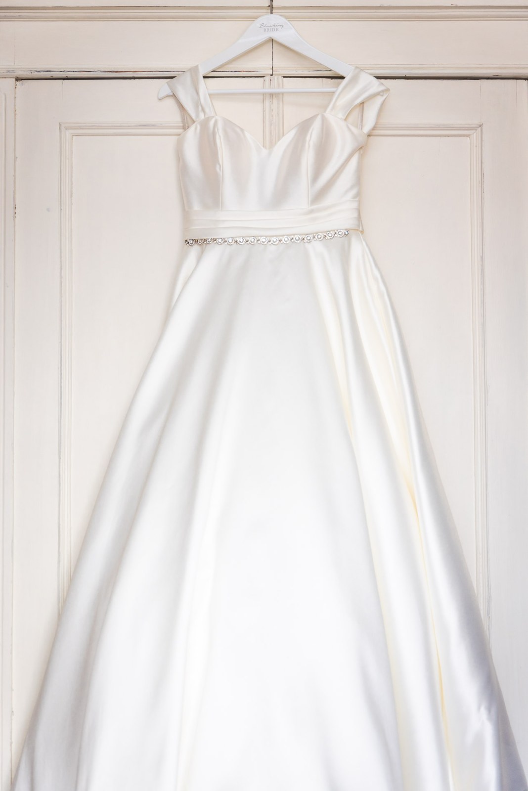 The bride's satin gown hanging on a panelled door
