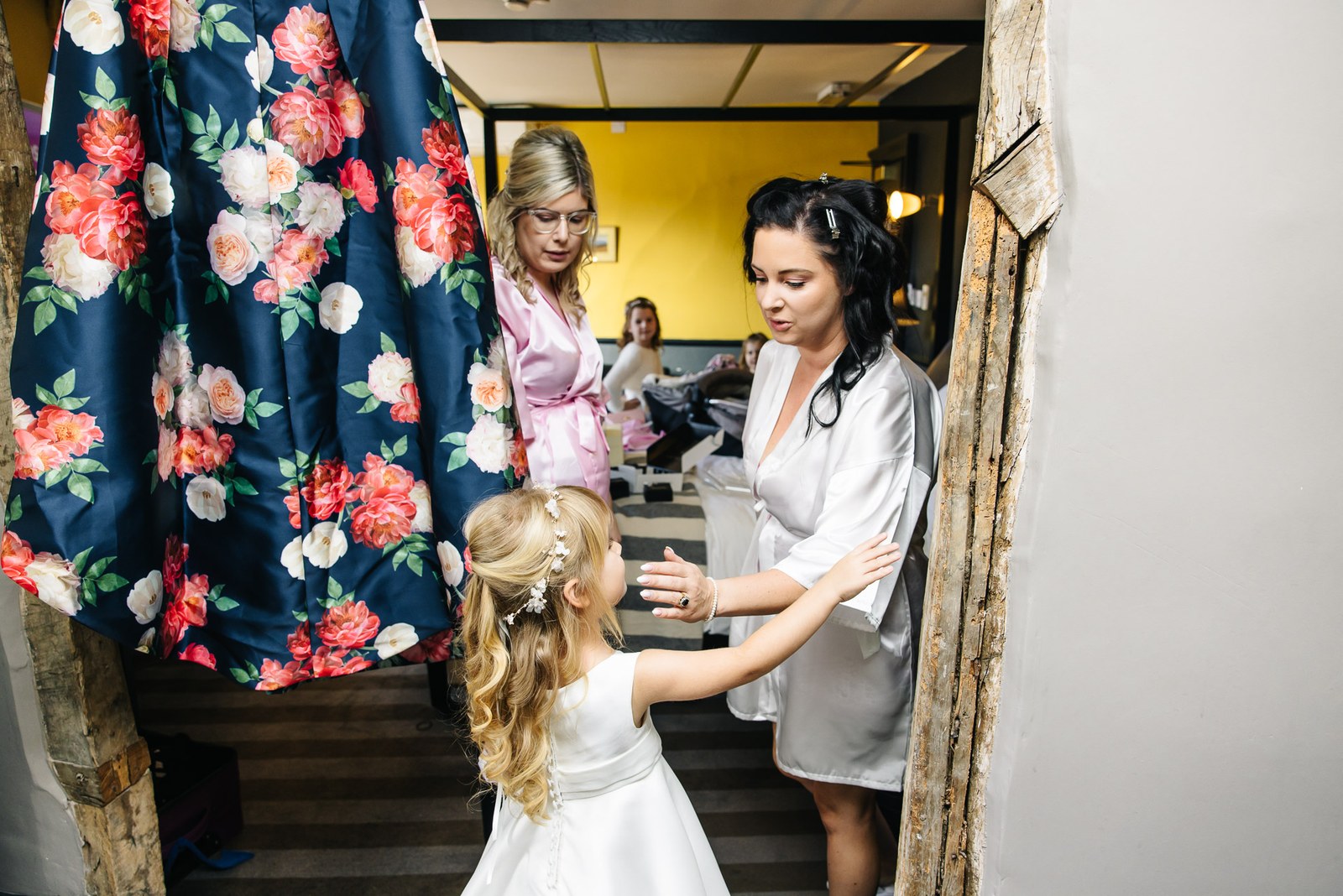 The bride in her robe steadies a flower girl on the stairs as a bridesmaid watches