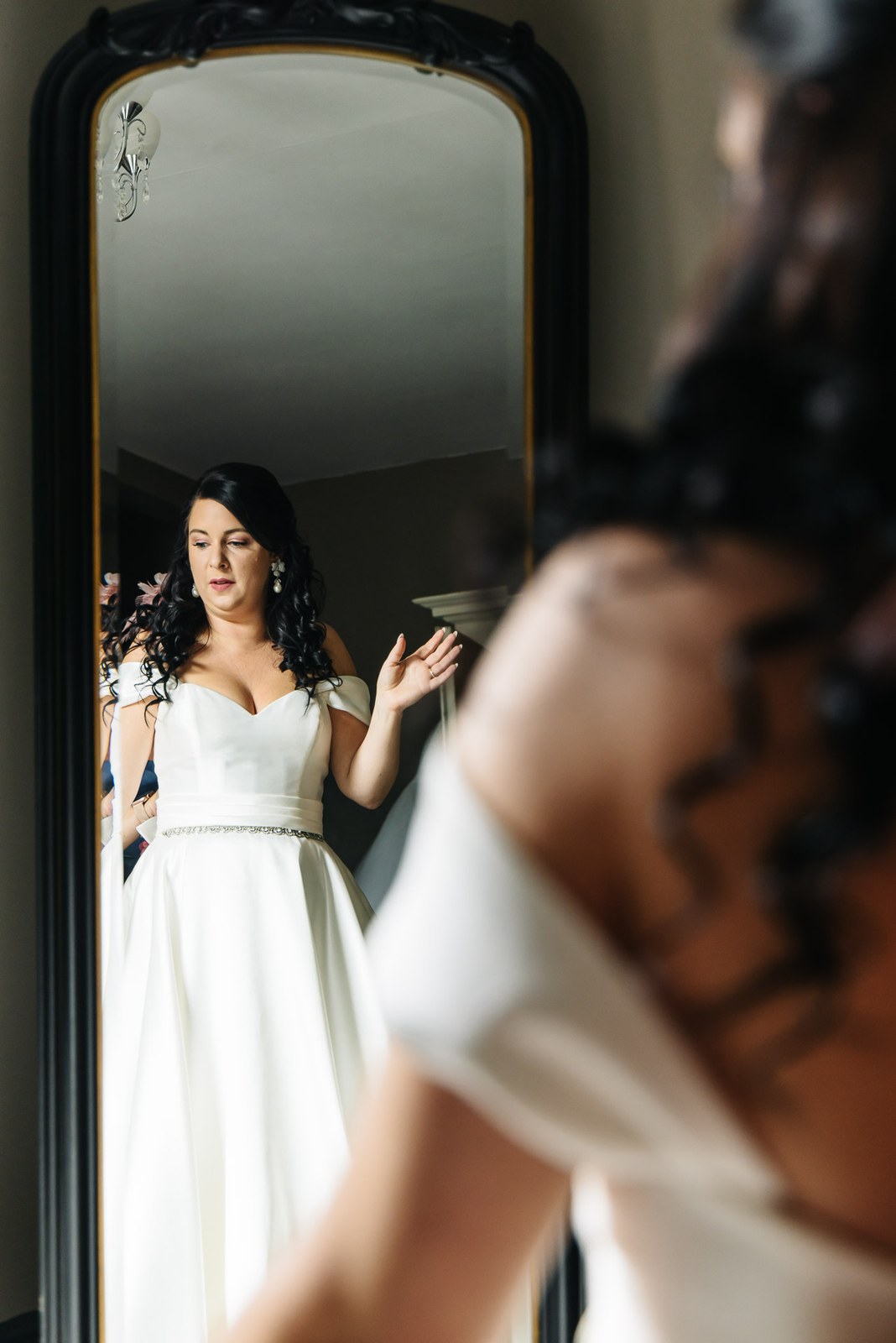 The bride adjusts her gown before a mirror as she gets ready