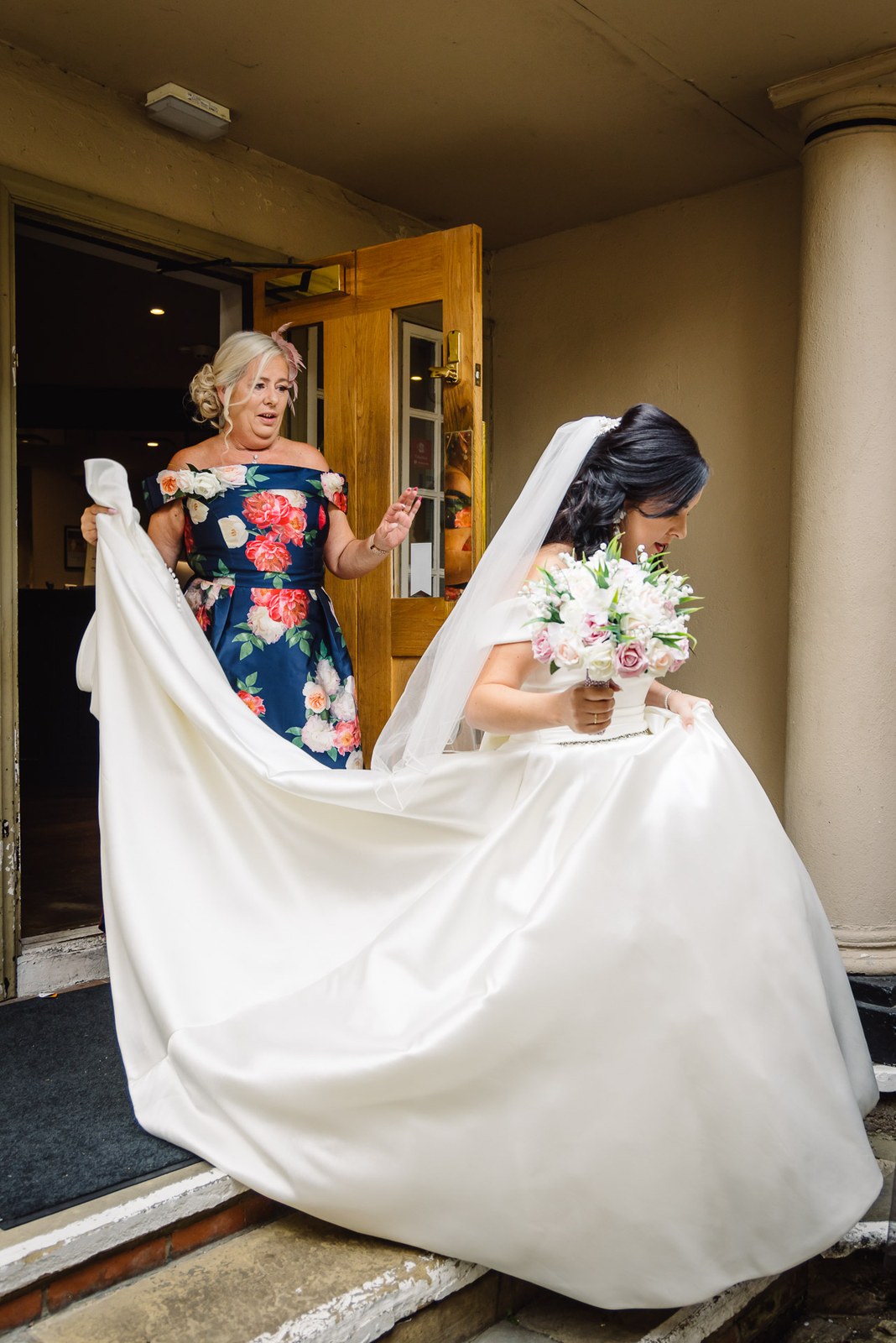 The bride's mother helps carry her long train as she steps through