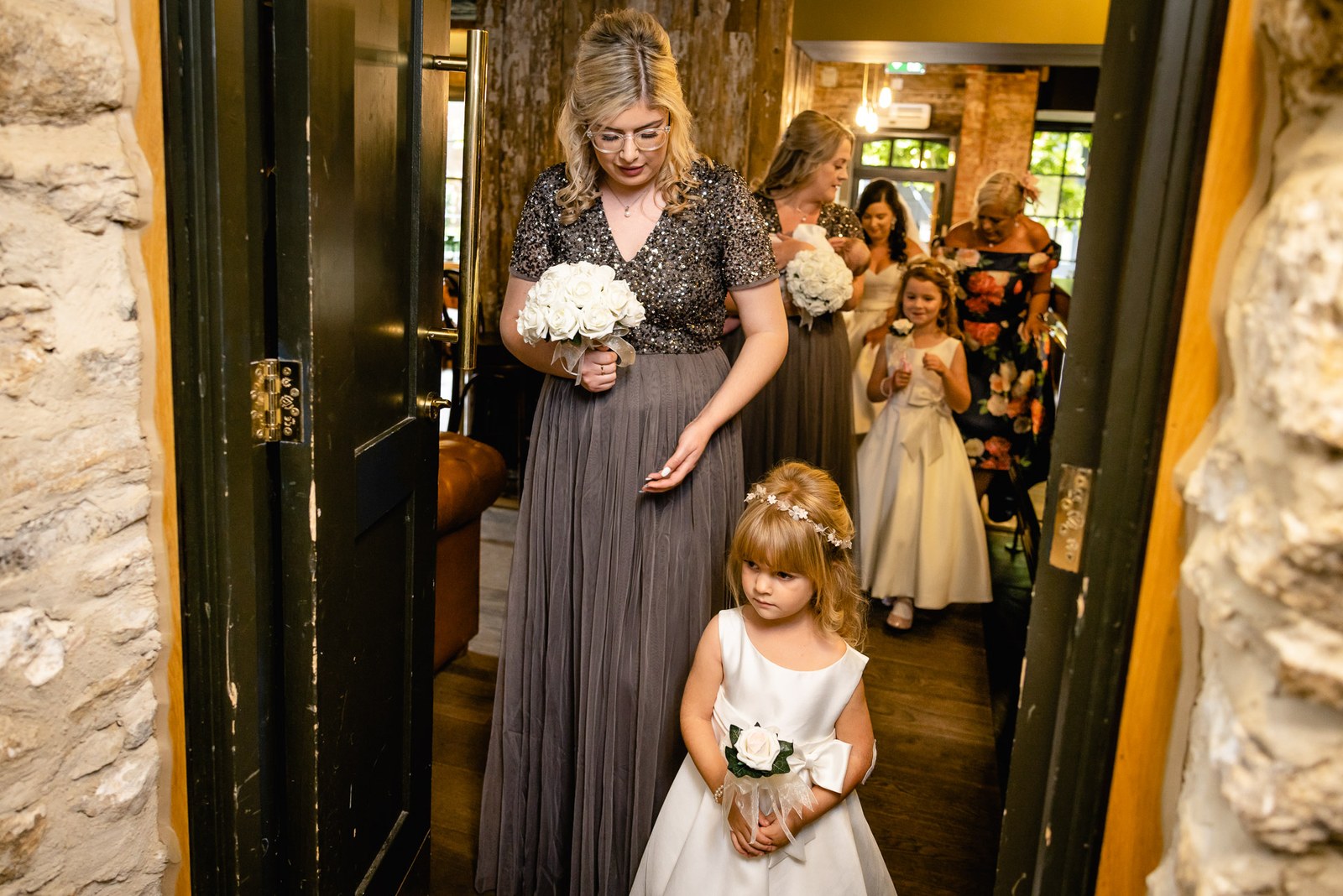 A bridesmaid and flower girl walk into the stone-walled ceremony room