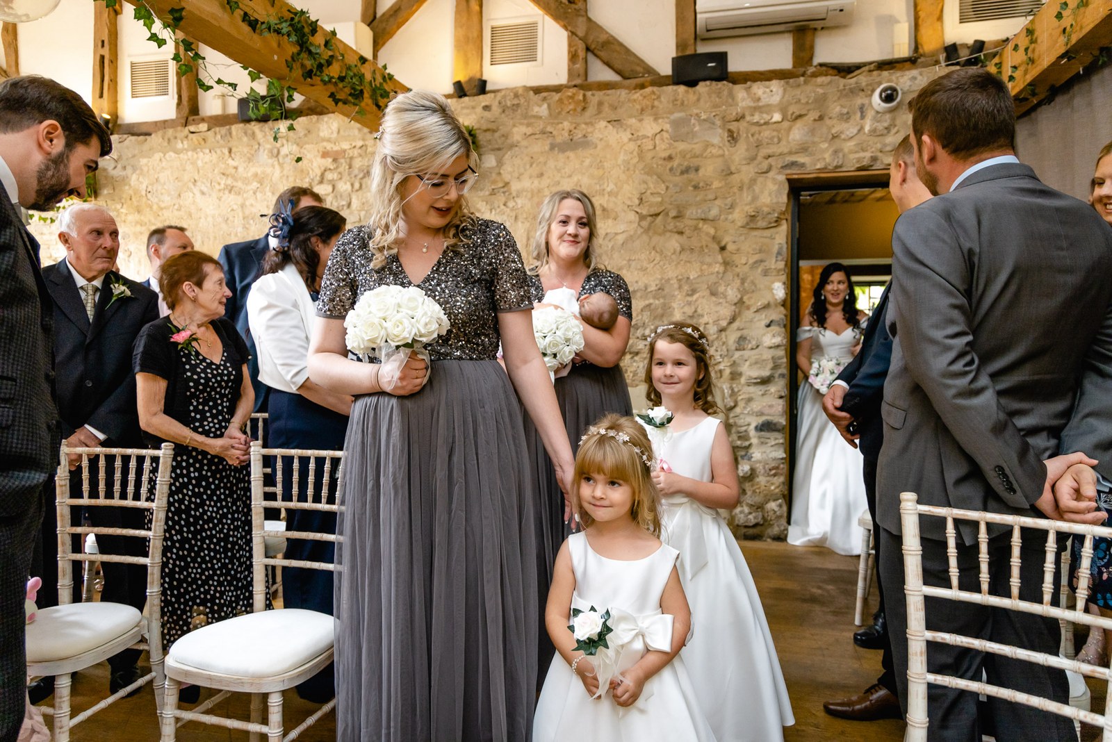 The bride arrives as guests stand in the beamed stone barn at the Crown & Thistle