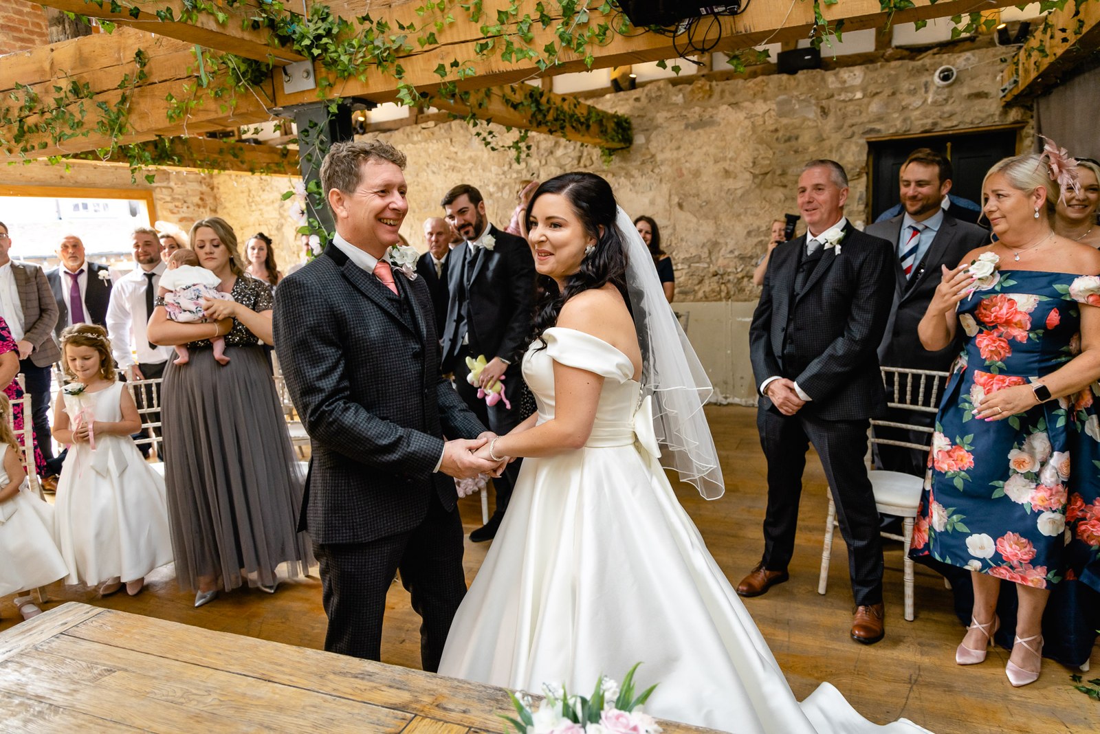 Bride and groom hold hands during the ceremony as guests look on