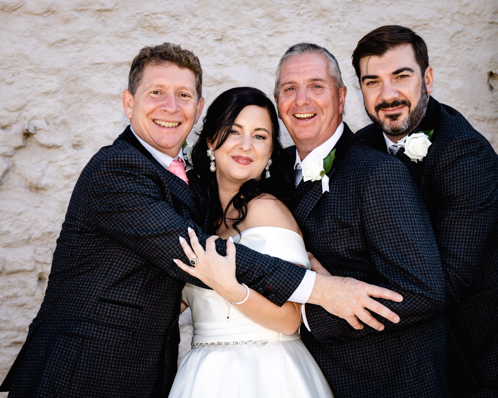 The bride is hugged by the groom and two men in matching checked suits
