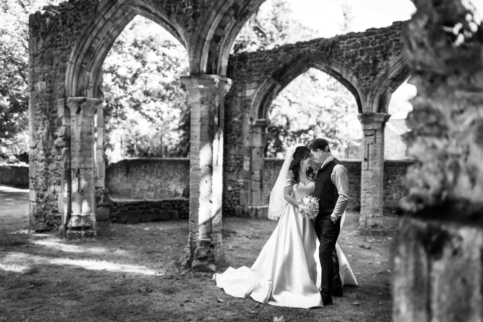 Black-and-white shot of the couple kissing beneath the arches of the abbey ruins