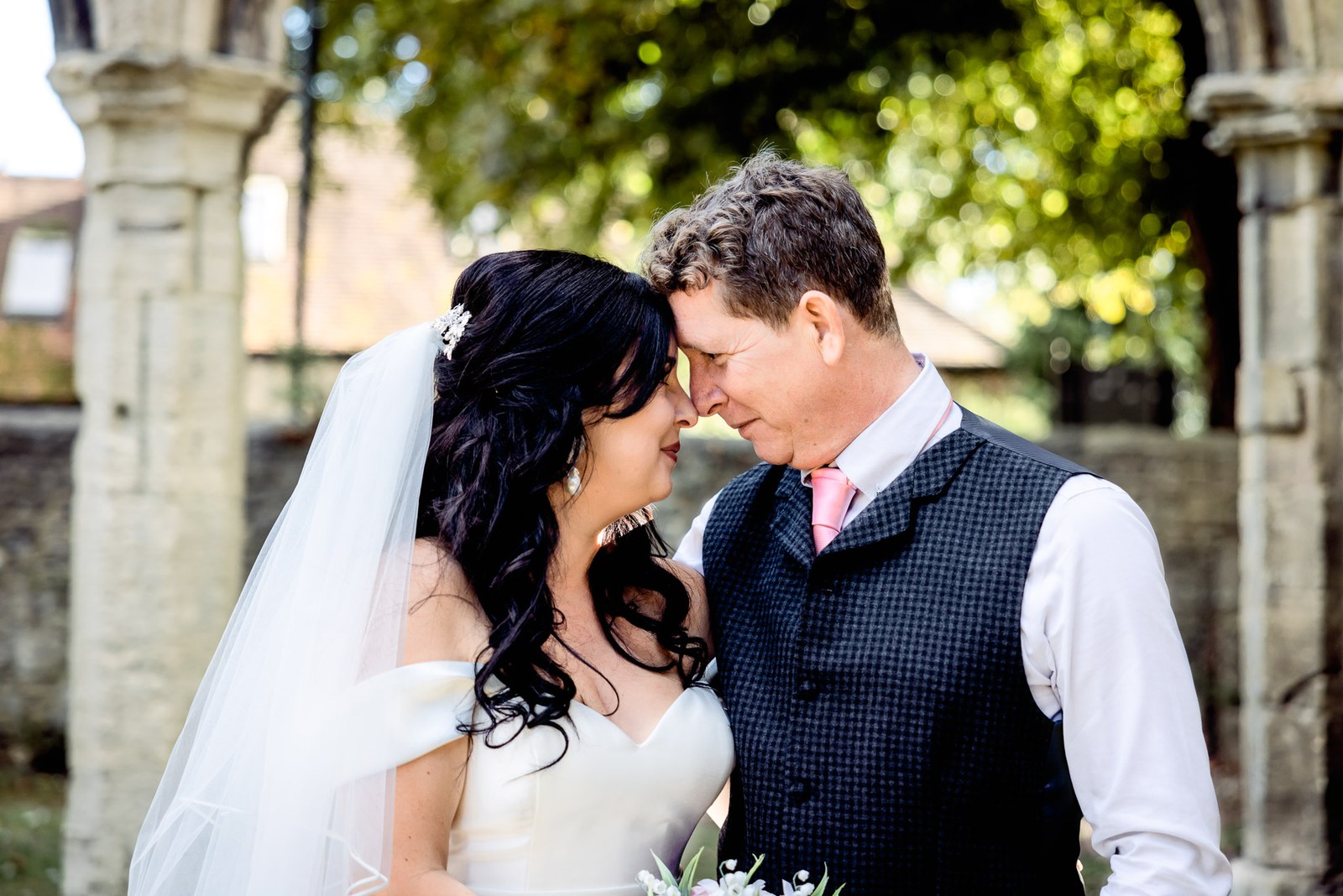 The couple rest forehead to forehead in the gardens by a stone pillar