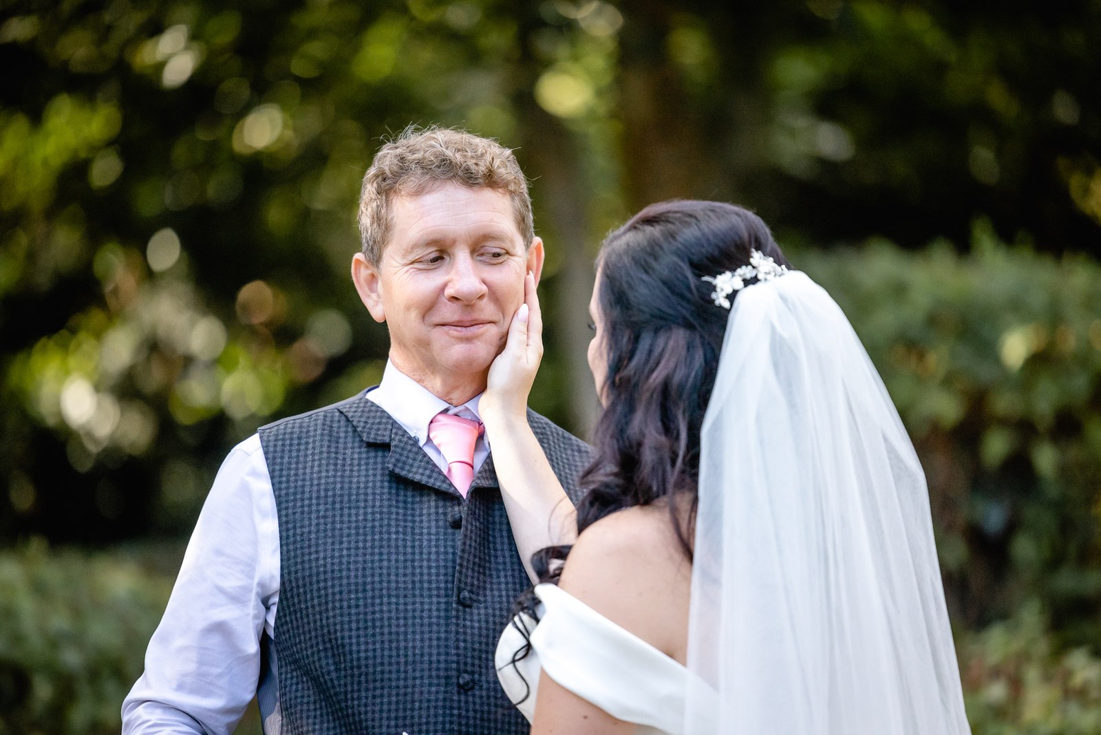 The bride cups the groom's face as they stand together in the garden