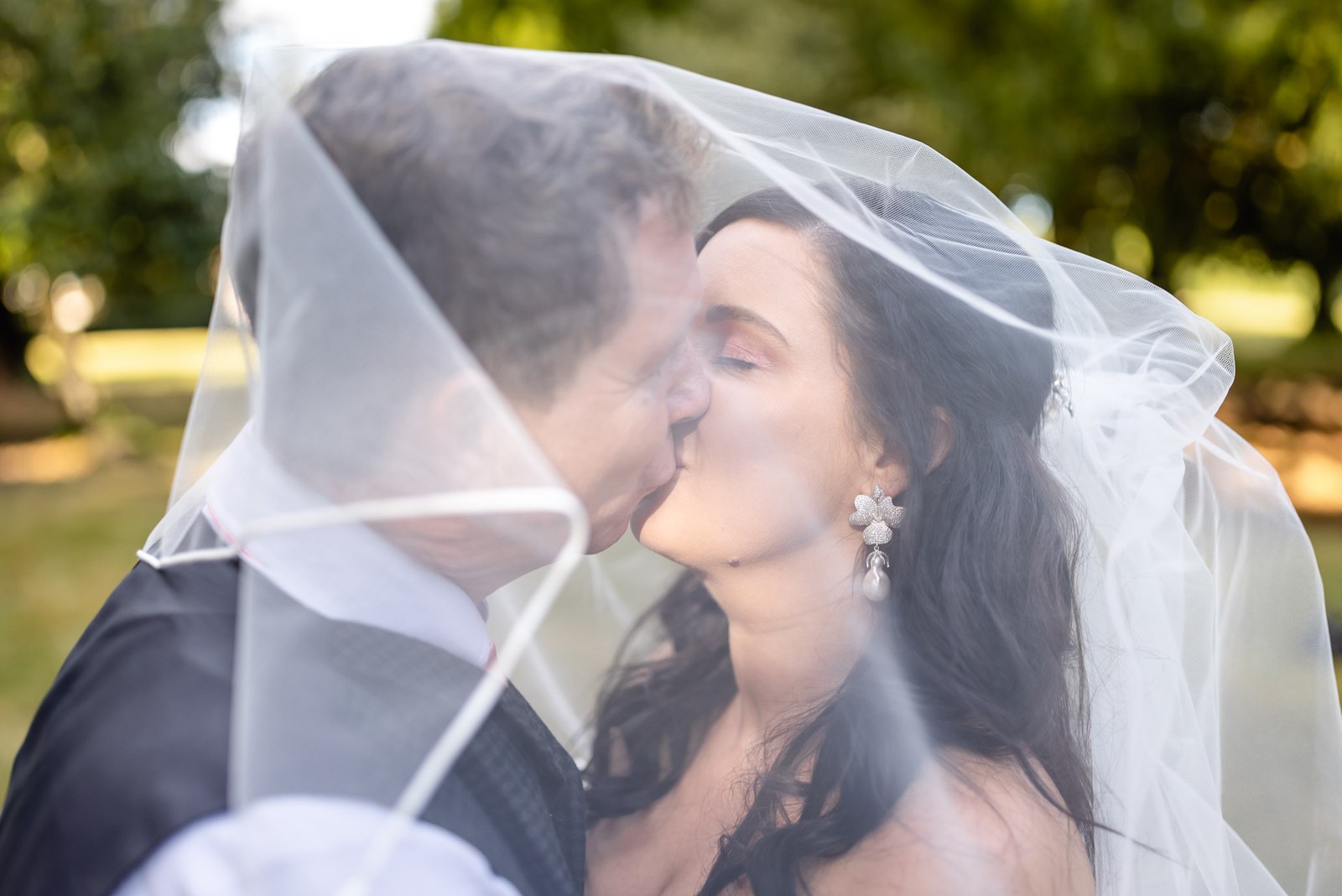The couple kiss beneath the bride's veil, her drop earrings showing