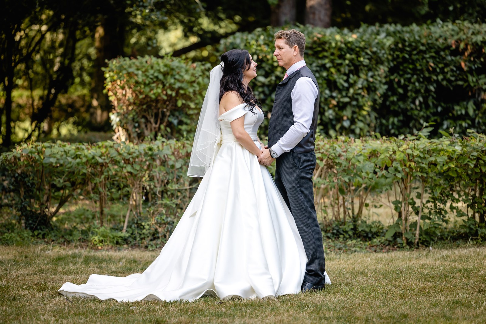 Bride and groom hold hands facing each other among the garden hedges