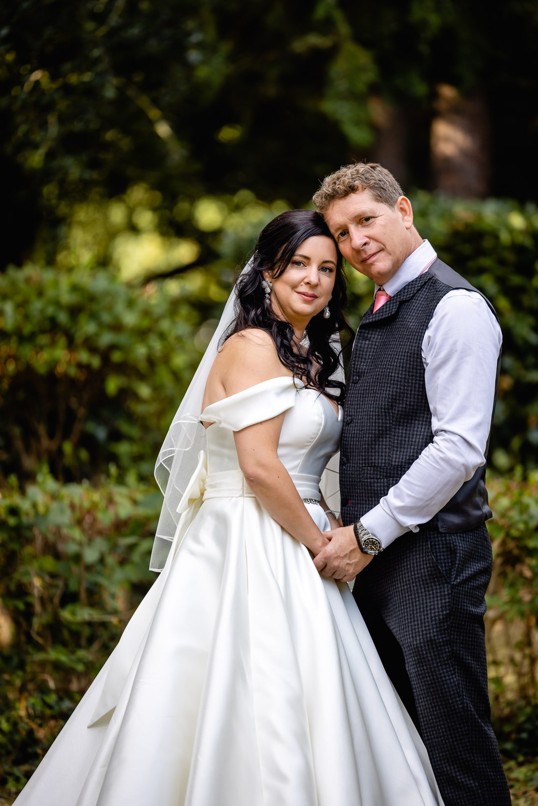 The bride leans into the groom for a portrait in the leafy garden