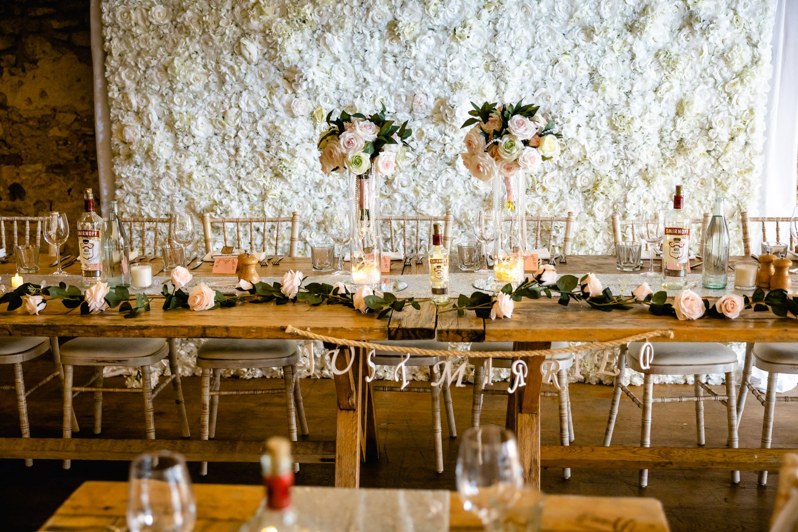 The reception tables at the Crown & Thistle dressed with pink roses before a white flower wall