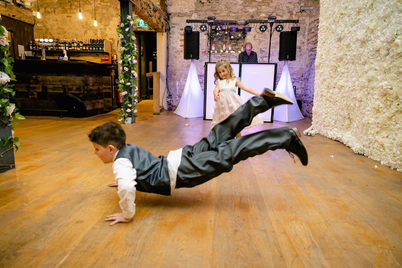 A page boy slides across the barn dancefloor as a flower girl watches