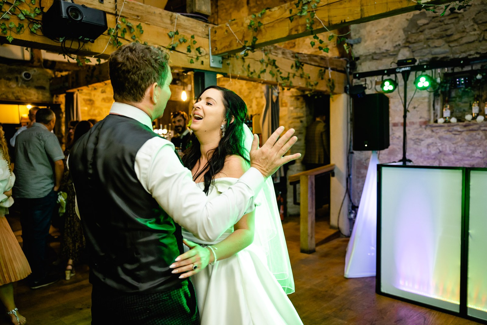 The couple share their first dance under green lights in the stone barn