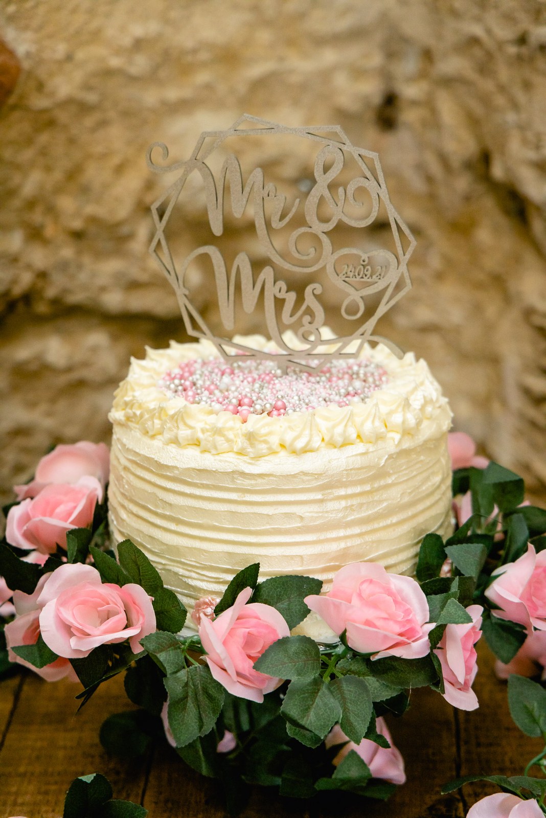 White wedding cake with a 'Mr & Mrs' topper ringed by pink roses