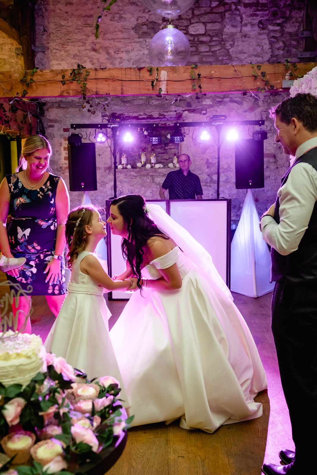 The bride dances with a flower girl beneath pink lights