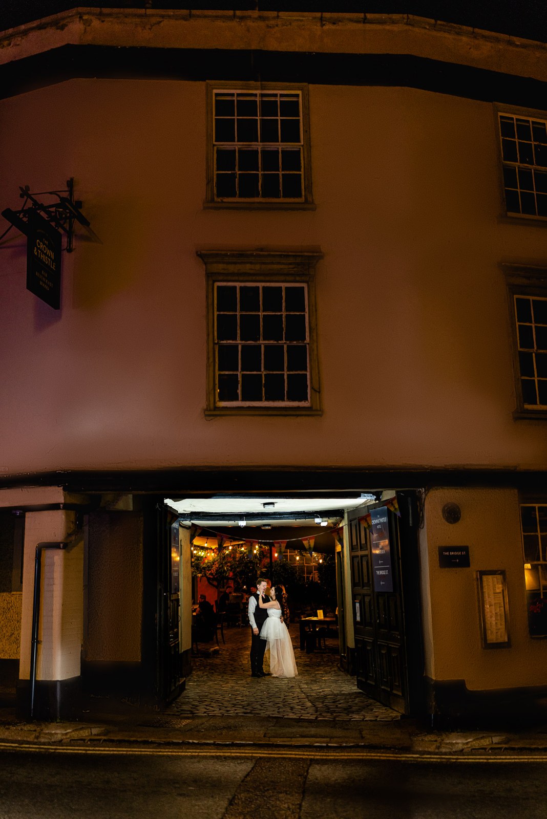 The couple framed in the lamplit archway of the Crown & Thistle at night