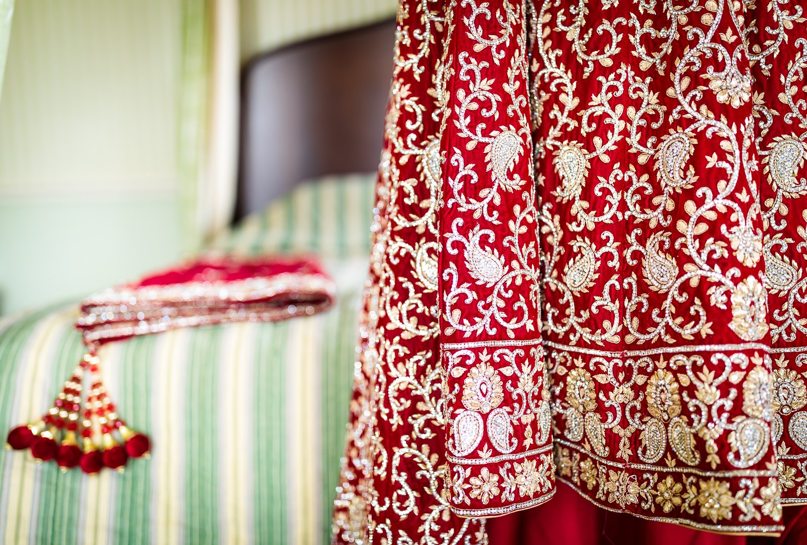 Richly embroidered red and gold bridal outfit hanging beside the bed