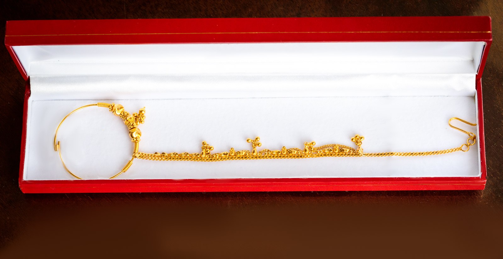 A gold maang tikka headpiece resting in a red presentation box
