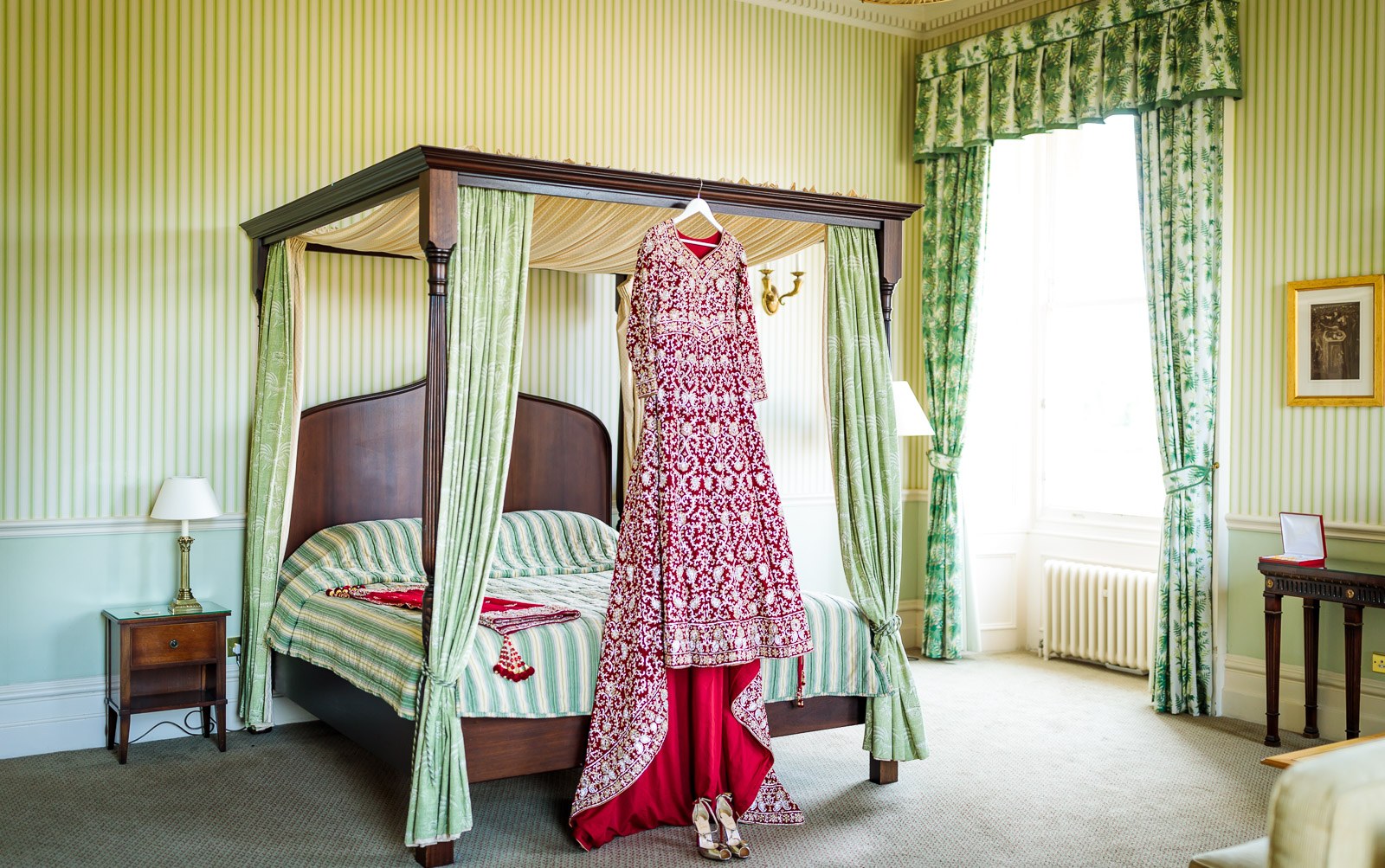 The red and gold bridal lehenga hanging on a four-poster bed at Heythrop Park