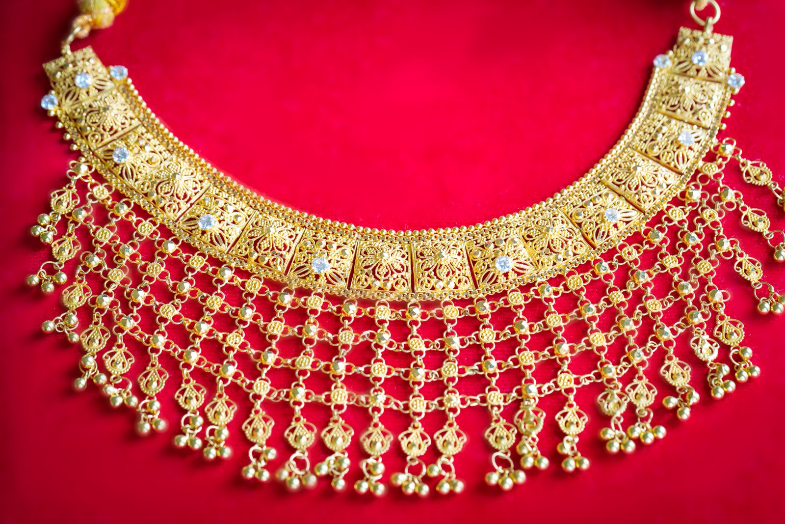 An ornate gold choker with hanging drops laid on red velvet
