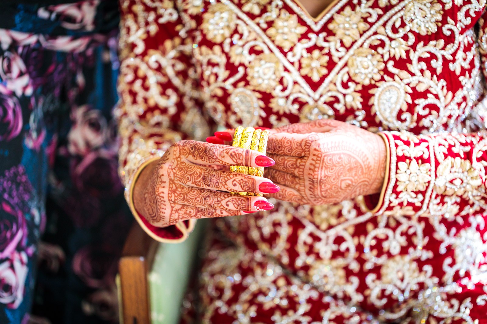 The bride's henna-decorated hand and gold bangles resting on her red outfit