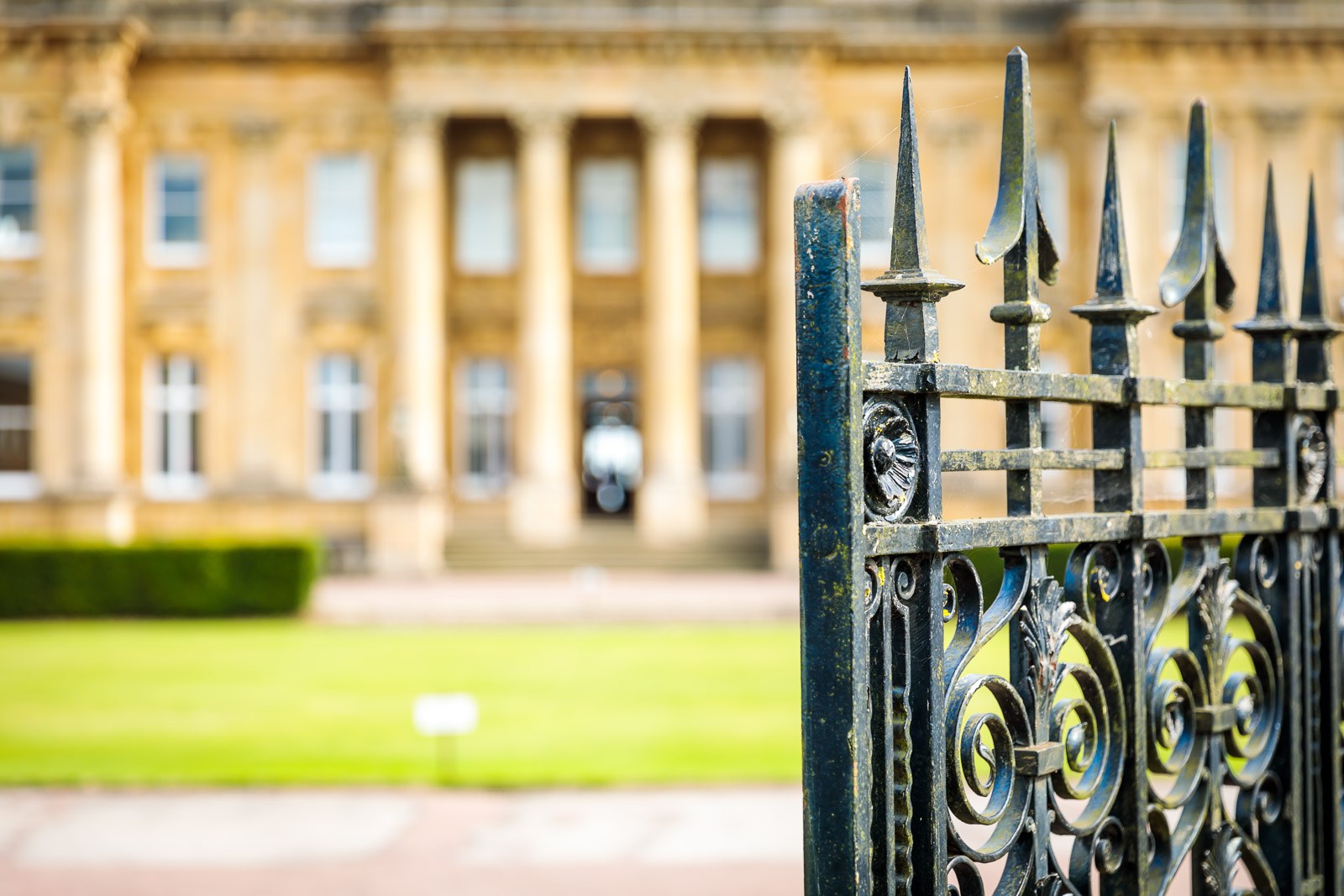 The honey-stone frontage of Heythrop Park glimpsed past a wrought-iron gate