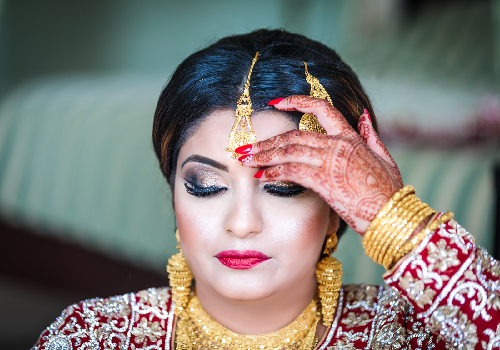 The bride touches her gold maang tikka, henna patterning her hand