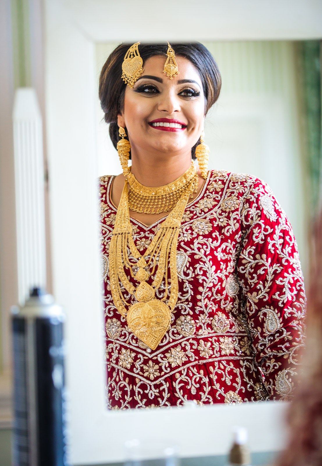 The bride studies her full red and gold bridal set in the mirror