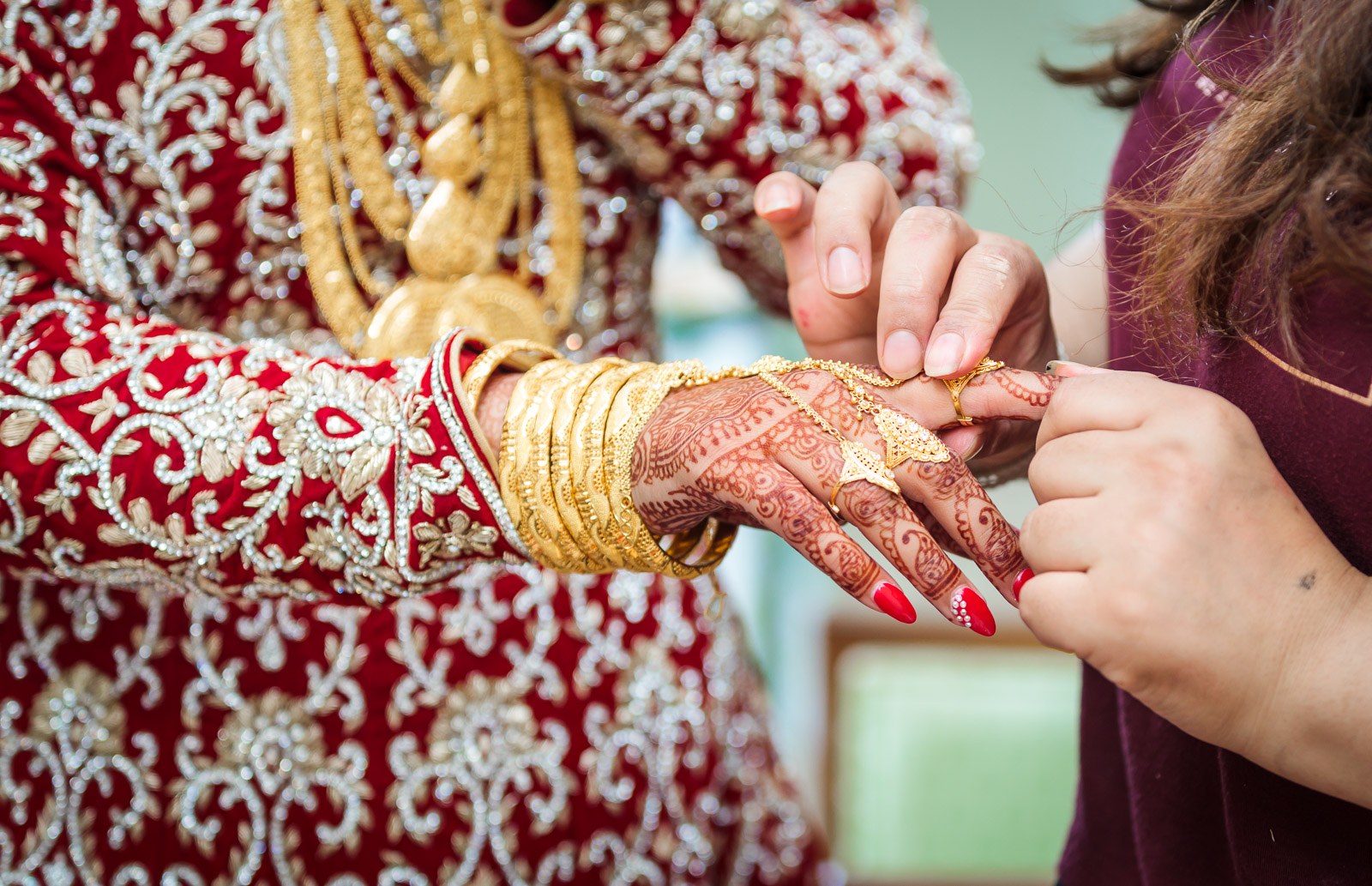 A helper slides a gold bangle onto the bride's henna-covered wrist
