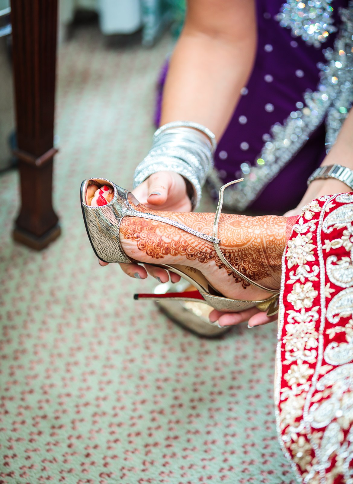 The bride's hennaed feet in gold heels being adjusted beneath her outfit