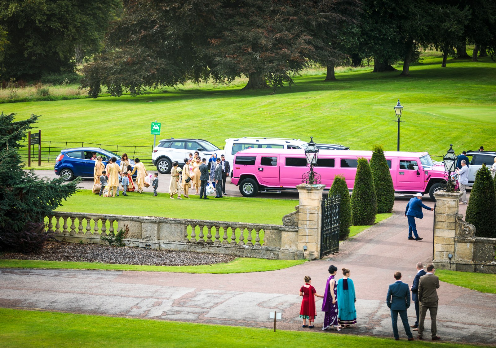 Elevated view of guests gathering by pink limousines on the Heythrop Park drive