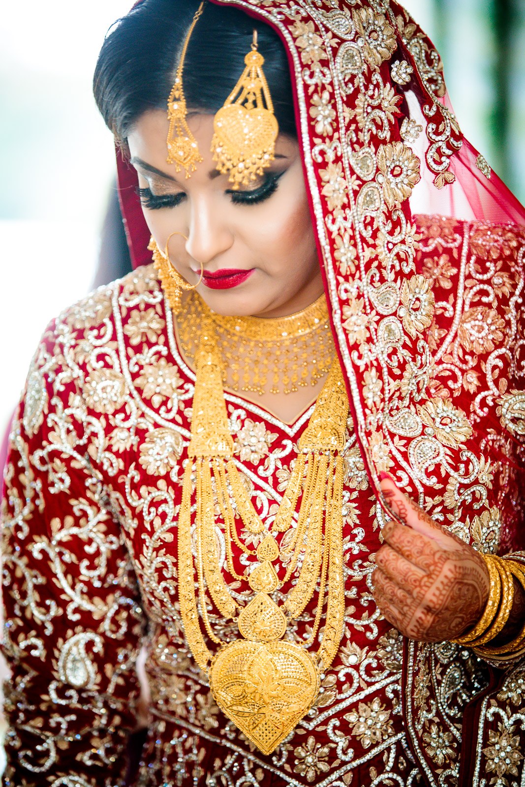 The bride in full red bridal wear and gold jewellery, looking down