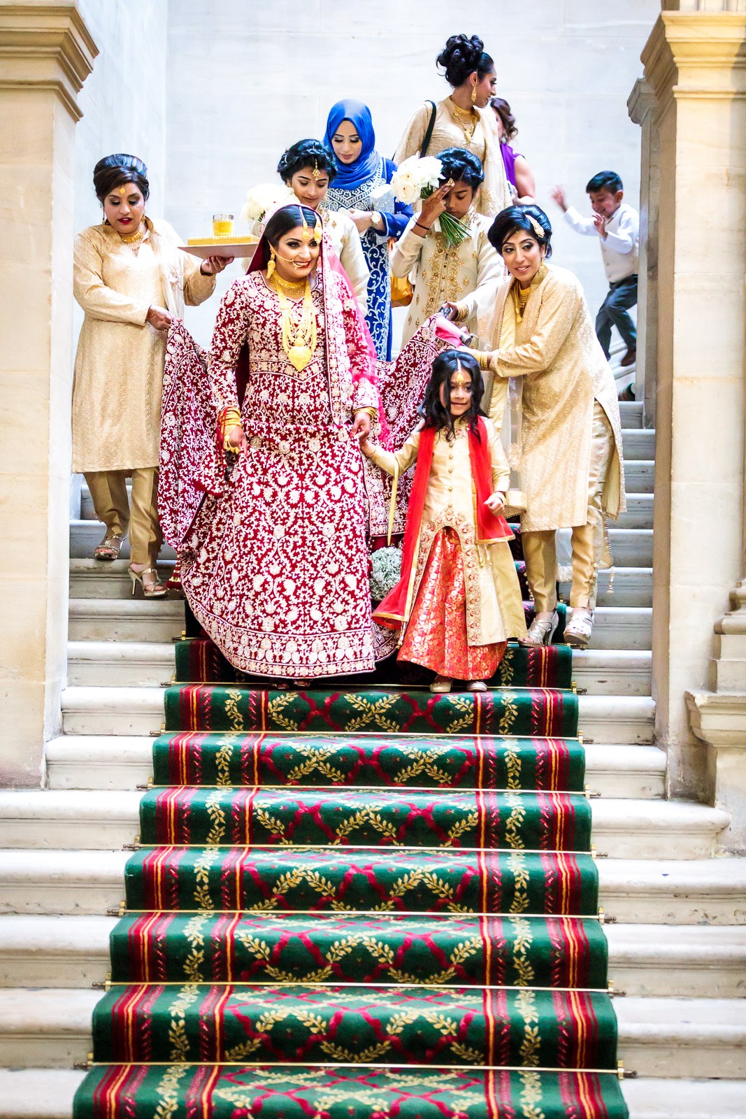 The bride is led down the garland-runnered grand staircase, helpers carrying her train