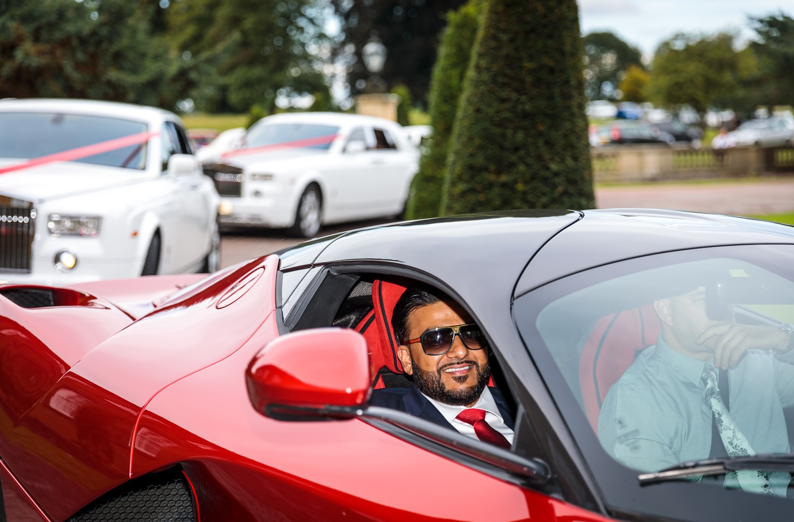 The groom sits in the red Ferrari behind a row of white Rolls-Royces