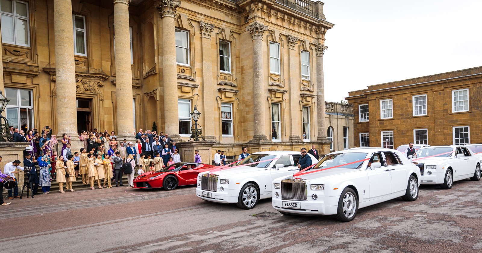 Wedding cars line the forecourt of Heythrop Park as guests gather on the steps