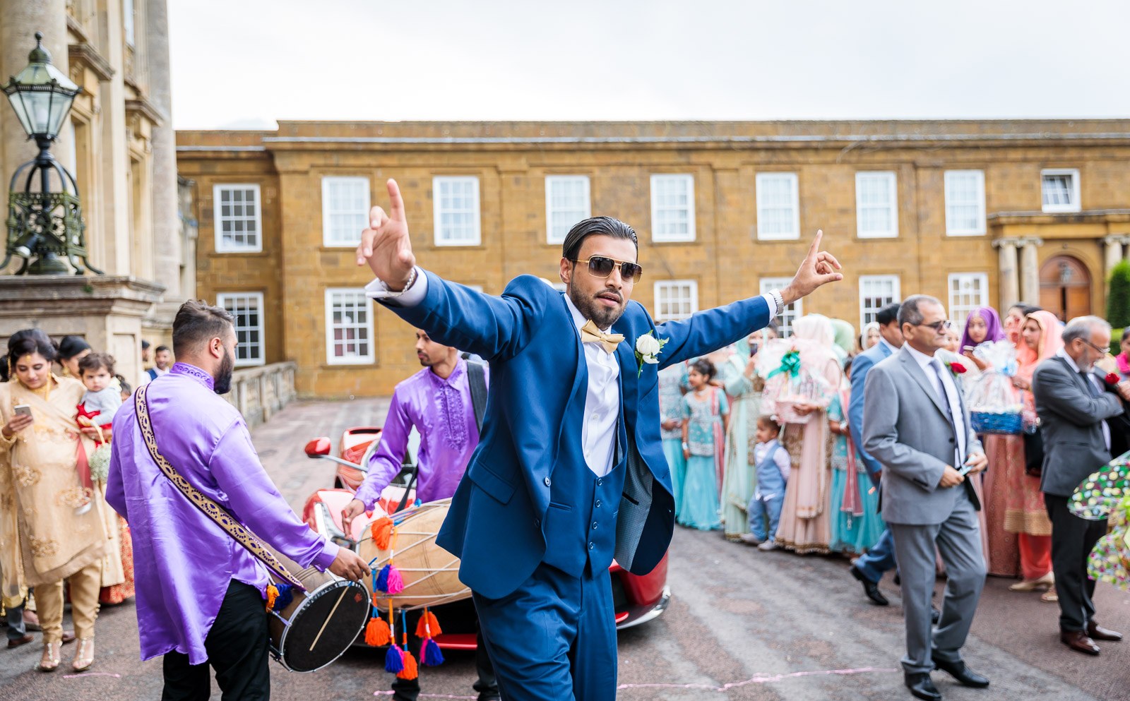 A guest in a blue suit dances with the dhol drummers in the courtyard