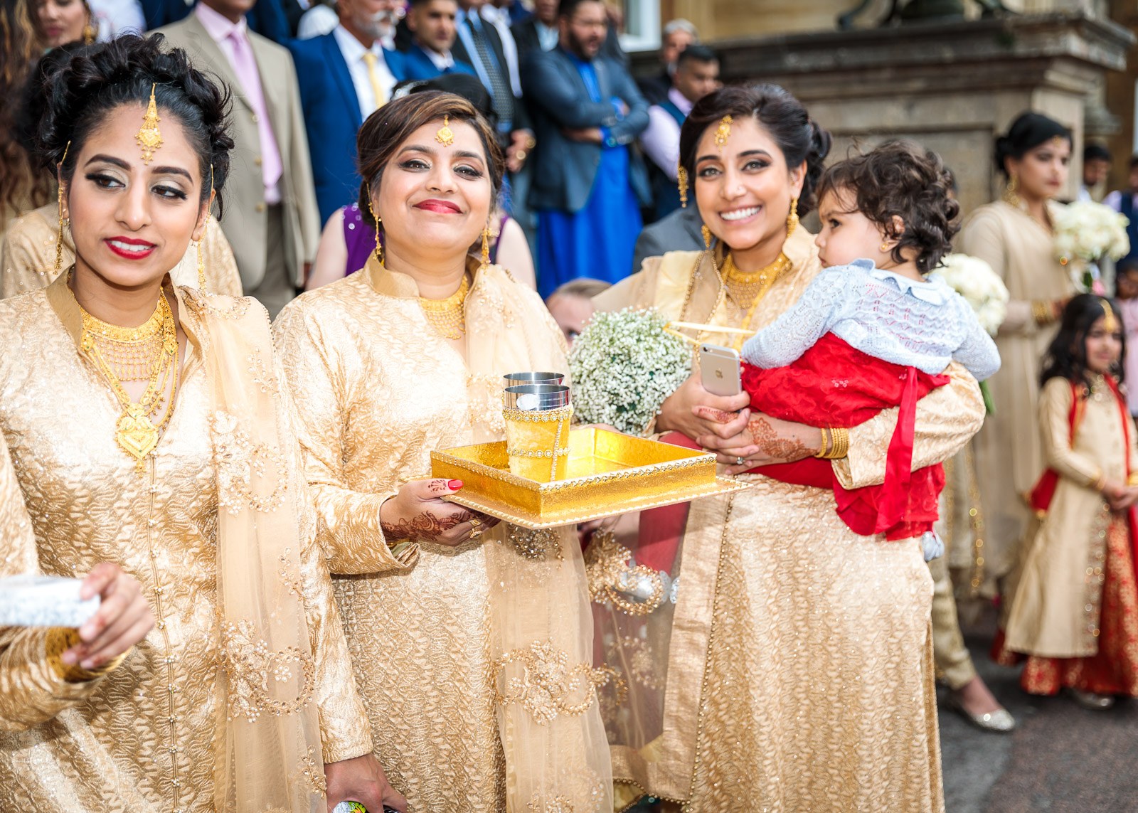 Women in gold carry welcome-drink trays through the arriving guests
