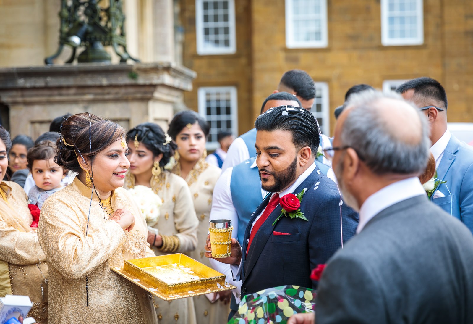 A woman in gold offers the welcome drinks as the groom takes a glass