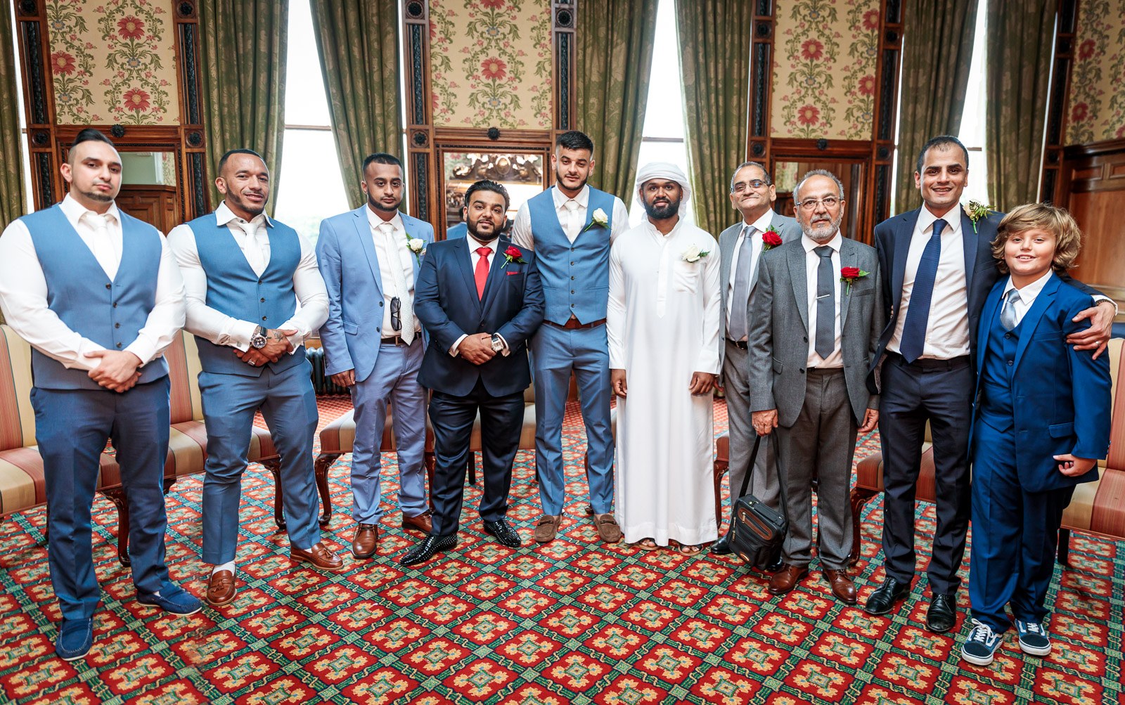 Groomsmen and elders gather in a floral-wallpapered room at Heythrop Park
