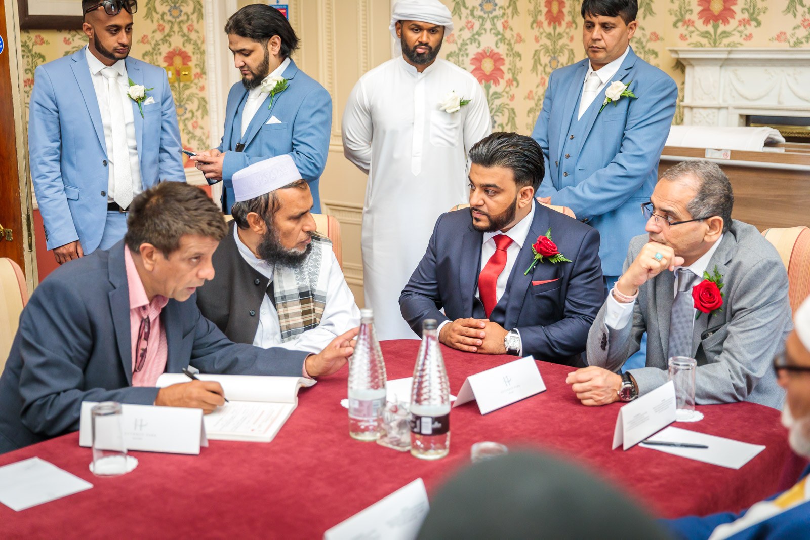 The men sign the nikah document at the table, the groom in navy