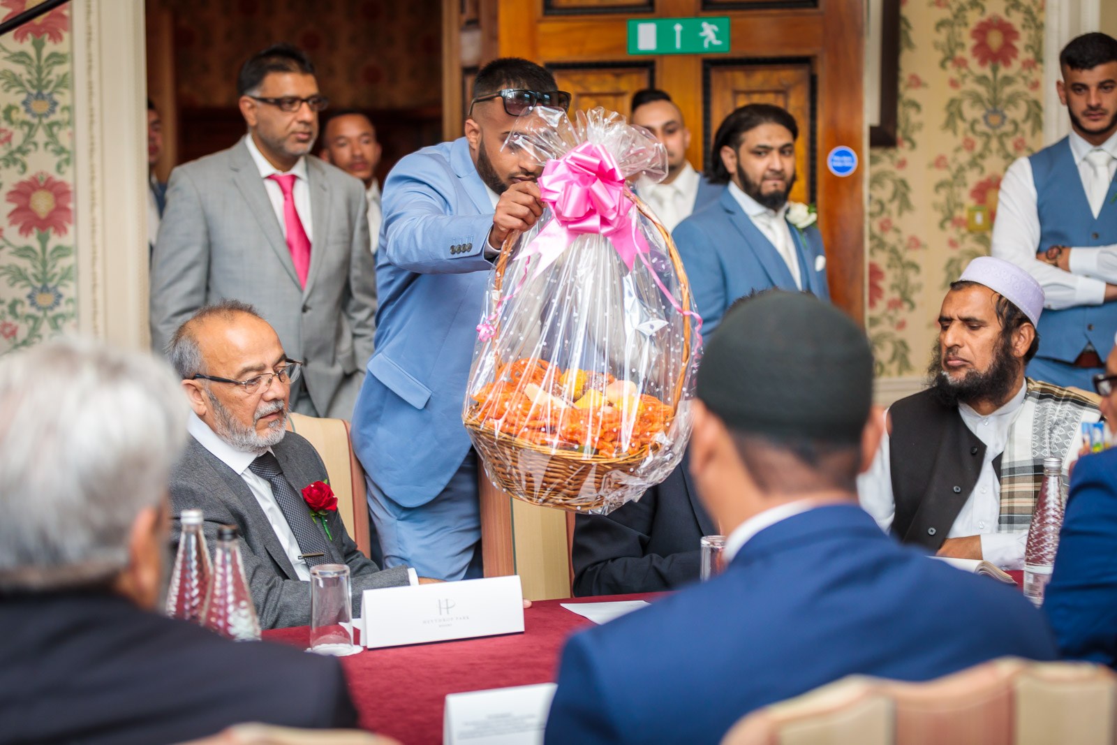 A guest presents a wrapped fruit basket to the seated elders